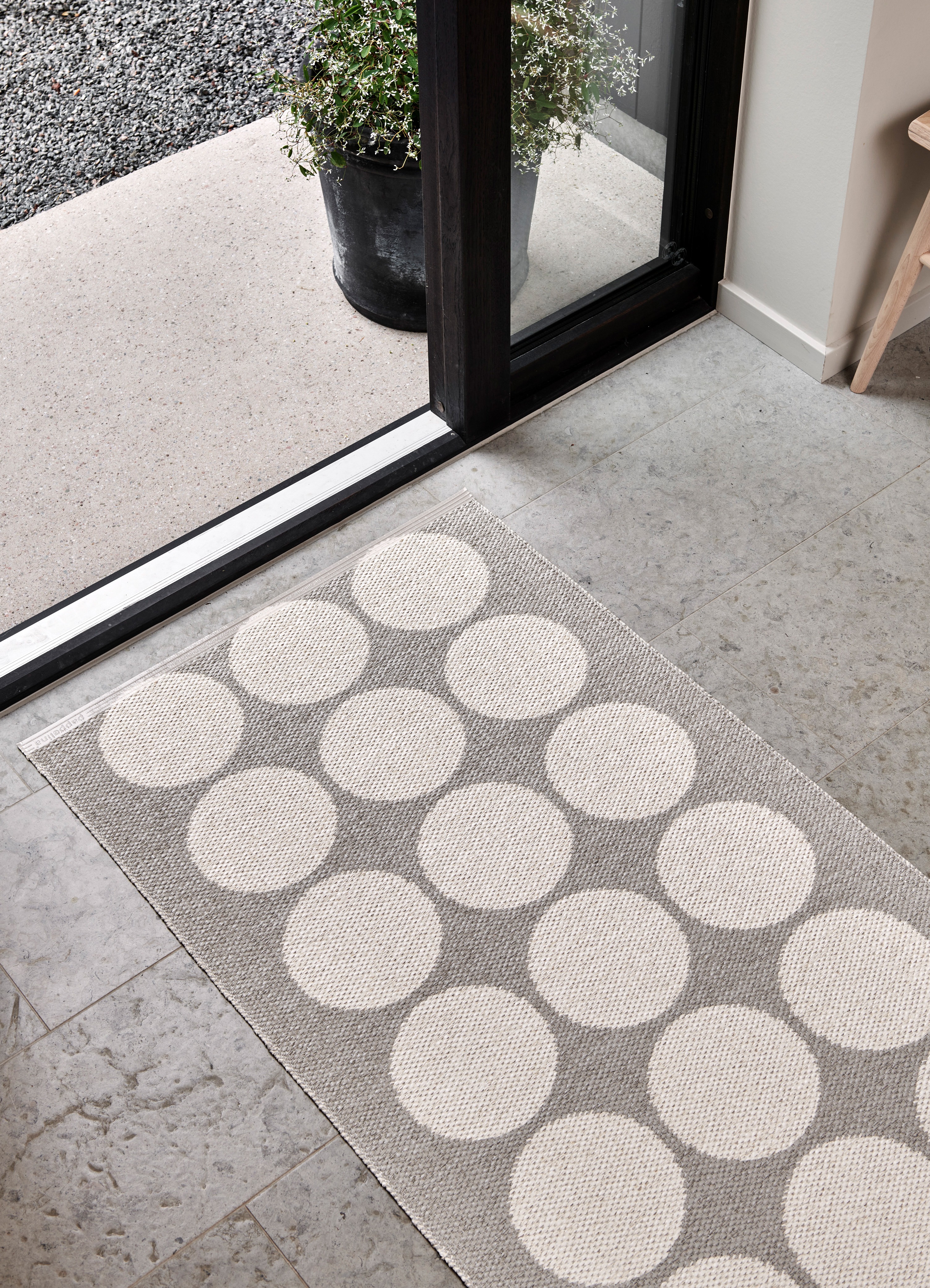 dotted grey tone rug on a stone floor in front of a glas slide door
